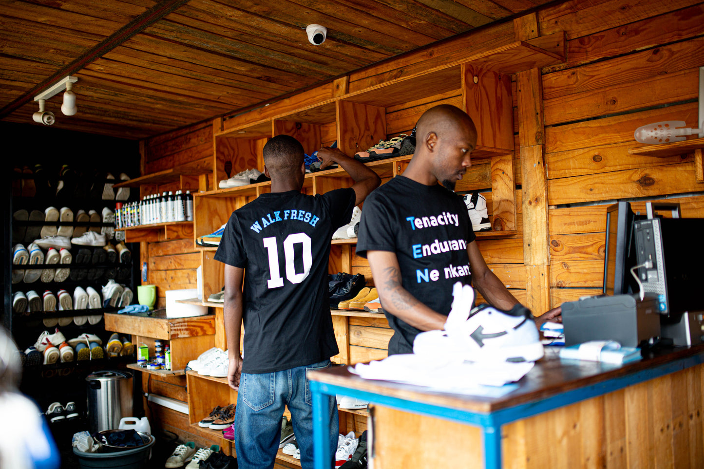 Two men working in a sneaker store wearing Walk Fresh t-shirts, showcasing shoe care and sneaker restoration.